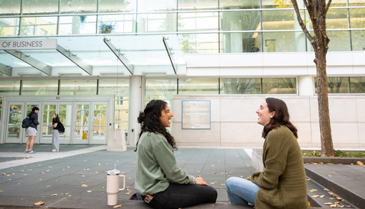 Two undergraduate students sit on a bench outside of the Scheller College of Business main entrance.