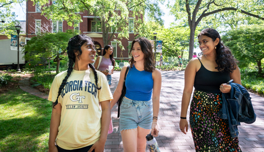 A group of students smile and laugh as they walk down a brick pathway on campus.